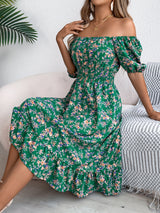 Abito estivo verde a fiori, spalle scoperte, indossato da donna seduta su sedia, stile casual elegante, moda femminile, tendenza 2023.