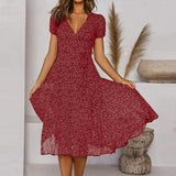 Donna con abito rosso a fiori, maniche corte, in posa elegante. Moda femminile estiva, stile casual chic. Sfondo neutro con decorazioni naturali.