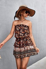 Donna con abito estivo floreale, cappello a tesa larga e occhiali da sole, posa contro un muro grigio. Moda estiva, stile boho-chic.